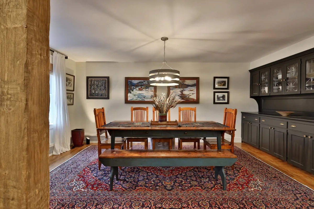 A spacious dining room featuring a large wooden table surrounded by chairs, decorative wall art, and dark cabinetry. The setting is ideal for shared meals, celebratory toasts, or group conversations, with warm lighting that enhances the cozy, communal atmosphere.