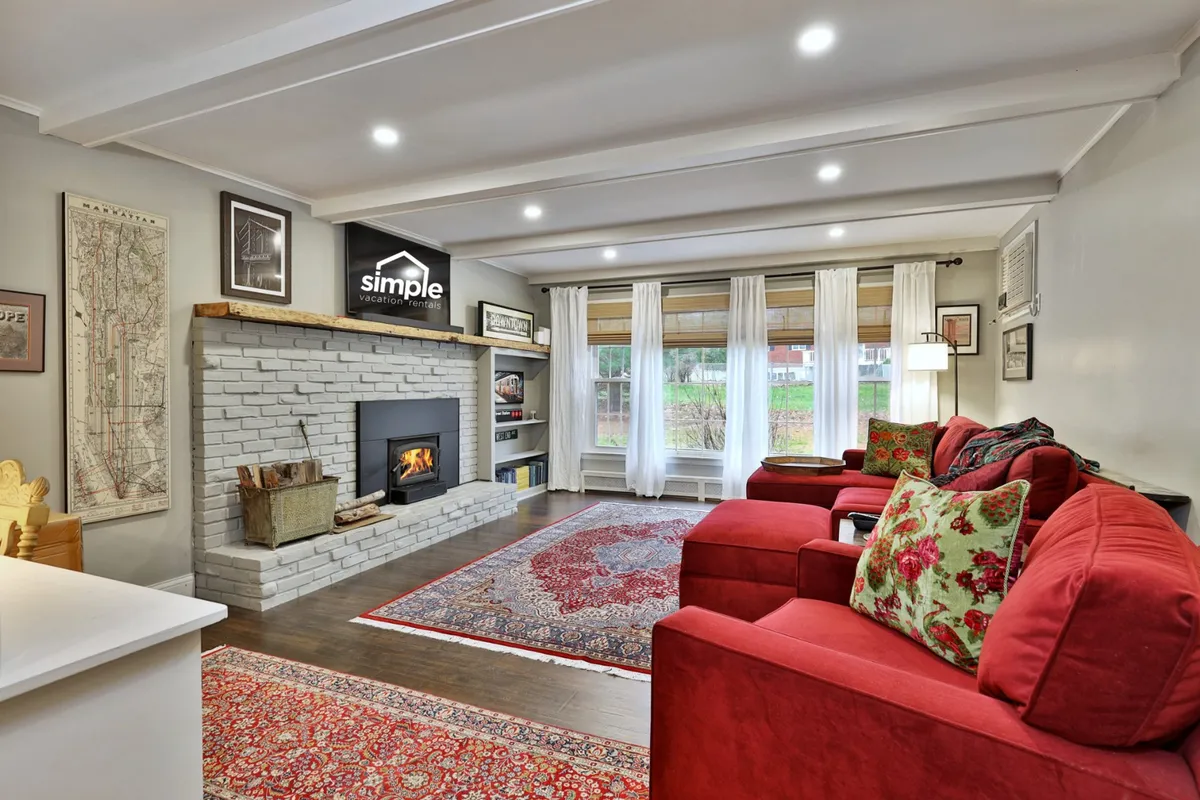 A cozy living room centered around a warm fireplace, with red sofas and an area rug inviting guests to gather. Large windows suggest natural light and views of the outdoors, creating an inviting space for après-ski story swapping or winding down after hiking and biking.