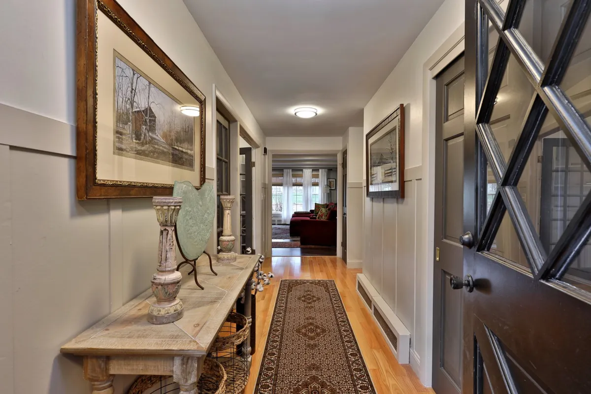 This image captures the home's entry area, featuring a vintage console table, framed artwork, and a decorative mirror that offer guests a warm, inviting welcome. The area rug and dark door provide a sense of comfort and personal history, setting the tone for family arrivals and departures.