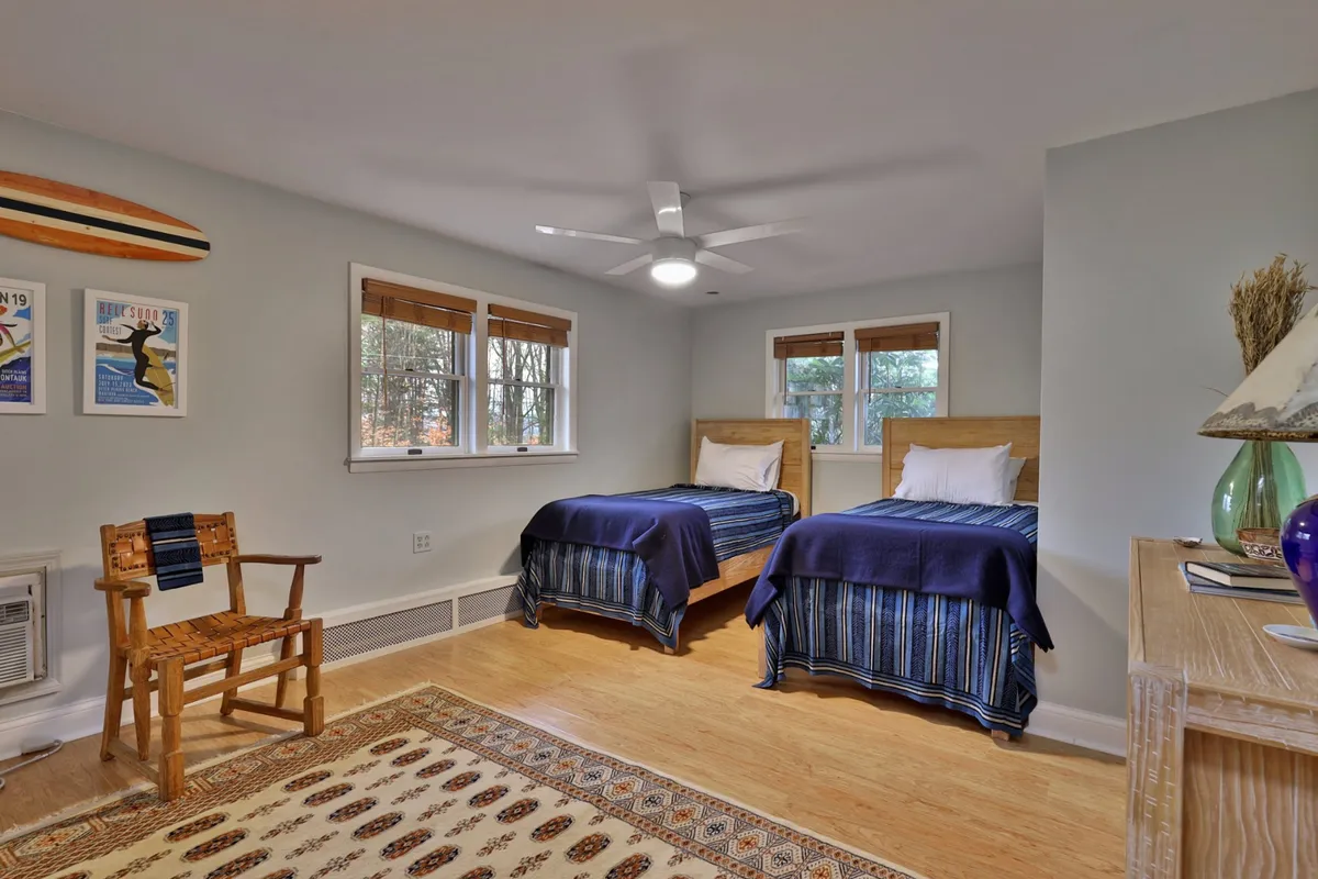 A cozy bedroom with two twin beds, a wooden chair, colorful artwork, and a decorative rug. The twin beds are positioned for optimal comfort and companionship, while playful touches and ample light create a cheerful, welcoming space.