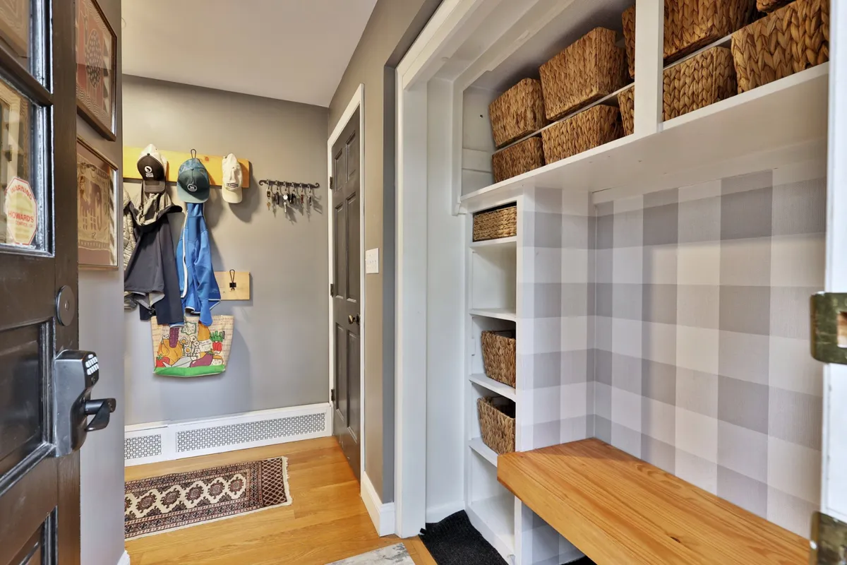 A tidy mudroom or entryway with coats neatly hung on hooks, woven baskets for storage, a cozy bench, and a decorative rug. The organized, inviting space immediately communicates a sense of order and welcome upon entering the home.