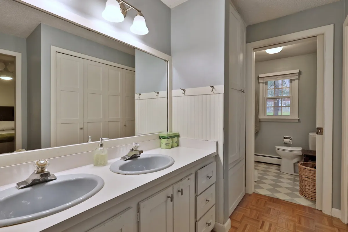 A calm, well-lit bathroom with double sinks, a mirrored cabinet, and neutral colored walls. The layout is functional for multiple guests getting ready simultaneously, making it ideal for pre-event preparations.