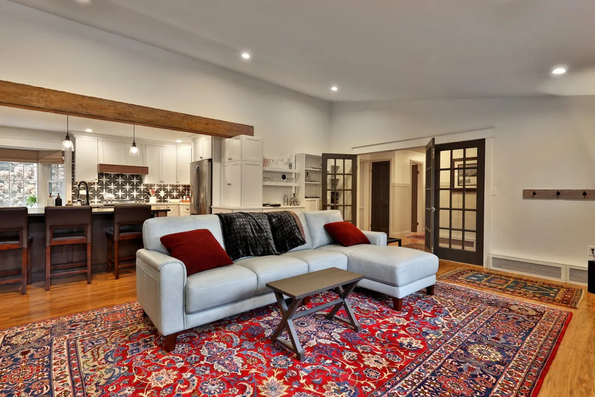 This image captures a cozy open-plan living space with a comfortable sofa, a stylish rug, a prominent kitchen island, and eye-catching light fixtures. The layout is designed to facilitate both relaxation and social gatherings, with the kitchen and living areas flowing seamlessly into one another.