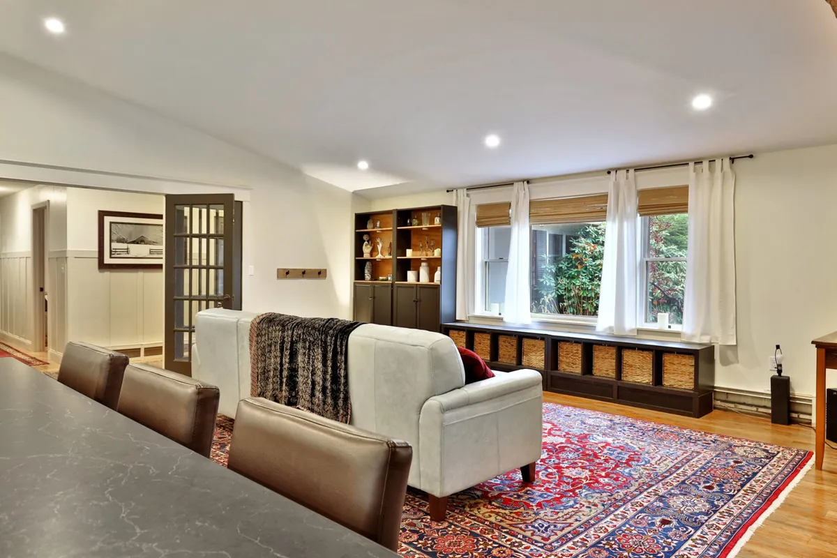 A welcoming living room scene featuring a comfortable sofa, a textured area rug, and a well-stocked bookshelf. Sunlight streams through the window, illuminating the cozy space and inviting guests to relax, socialize, or enjoy intimate conversations.