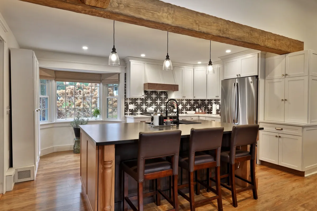The image highlights a warm, welcoming kitchen with a spacious island, pendant lights, and attractive backsplash tile. The space is designed for cooking, entertaining, and family gatherings, inviting guests to share recipes or prep for group outings.
