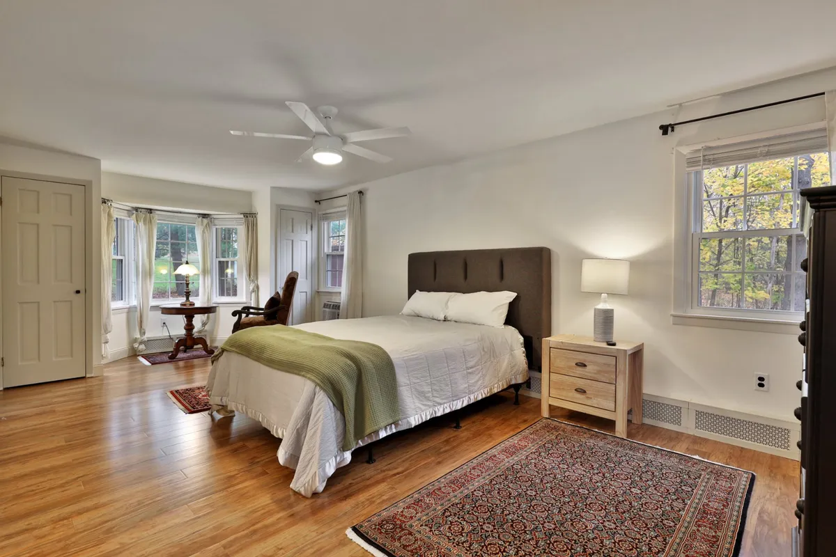 A tranquil bedroom with a cozy bed, a comfortable chair beside a window, a soft rug, and a warm lamp casting gentle light. The atmosphere is restful and private, ideal for quiet evenings and restful sleep.