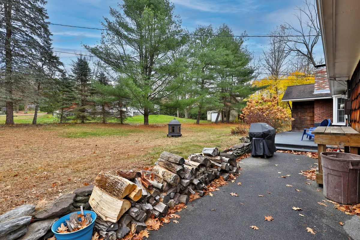 This image features a charming outdoor seating area beside a stacked pile of firewood and a grill, all set against a lush natural backdrop. The space looks ready for barbecuing, friendly gatherings, and relaxed evenings by the fire pit.