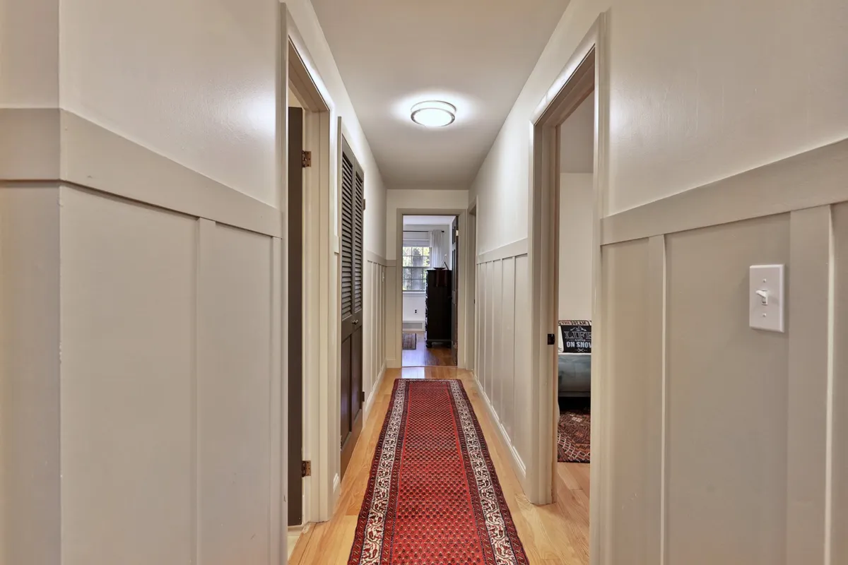 A long, inviting hallway with a decorative runner rug and open doorways leading into various rooms, evoking the sense of arrival and movement through the home. The light and sightlines suggest openness and a welcoming atmosphere.